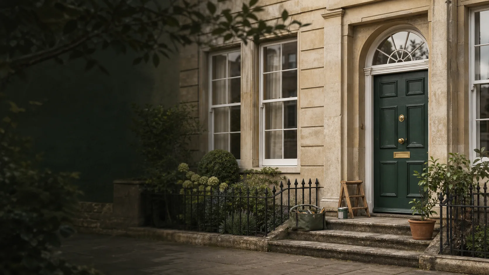Illustrative Bath-style stone home with a green front door and a small tool bag, reused from the AHAH homepage; not a completed-work photograph.